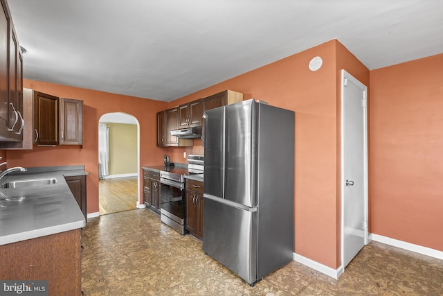 kitchen featuring a sink, under cabinet range hood, arched walkways, appliances with stainless steel finishes, and baseboards