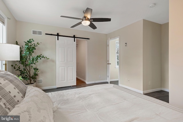 unfurnished bedroom featuring a barn door, visible vents, baseboards, and wood finished floors