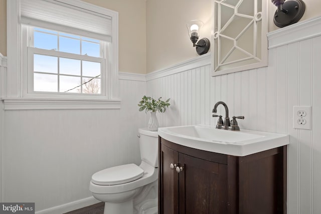 half bathroom with a wainscoted wall, toilet, and vanity