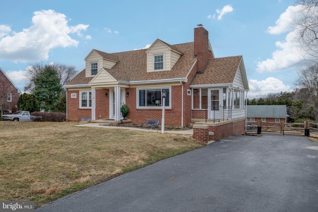 cape cod house with brick siding, fence, roof with shingles, a chimney, and a front yard