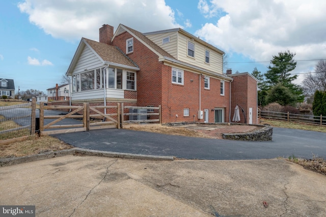 view of property exterior with brick siding, a chimney, fence, and a gate