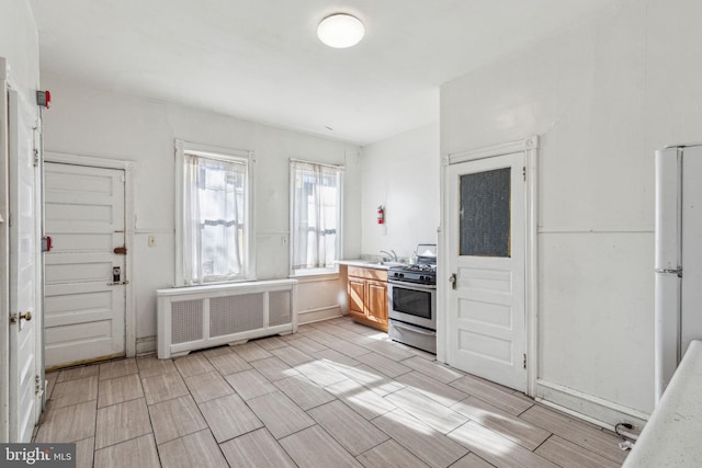 kitchen with light countertops, radiator heating unit, freestanding refrigerator, a sink, and gas range