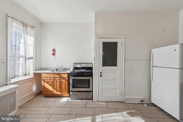 kitchen featuring brown cabinetry, radiator, freestanding refrigerator, stainless steel gas range, and a sink