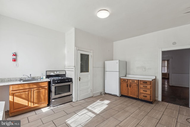 kitchen featuring brown cabinetry, freestanding refrigerator, stainless steel gas range, light countertops, and wood finish floors