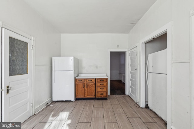 kitchen featuring light countertops, wood tiled floor, freestanding refrigerator, and brown cabinets