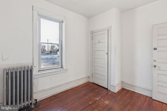 unfurnished room featuring dark wood-style floors, baseboards, and radiator