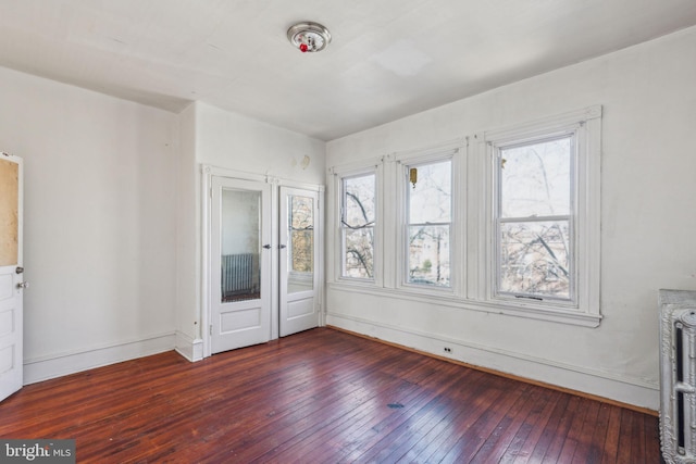 unfurnished bedroom with wood-type flooring, multiple windows, baseboards, and radiator heating unit