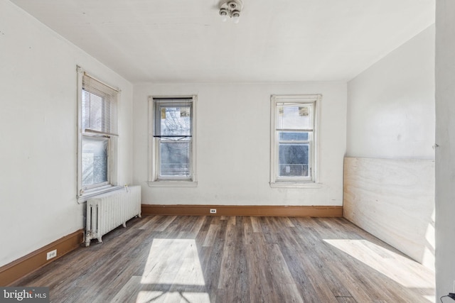 unfurnished room featuring baseboards, a healthy amount of sunlight, radiator heating unit, and wood finished floors