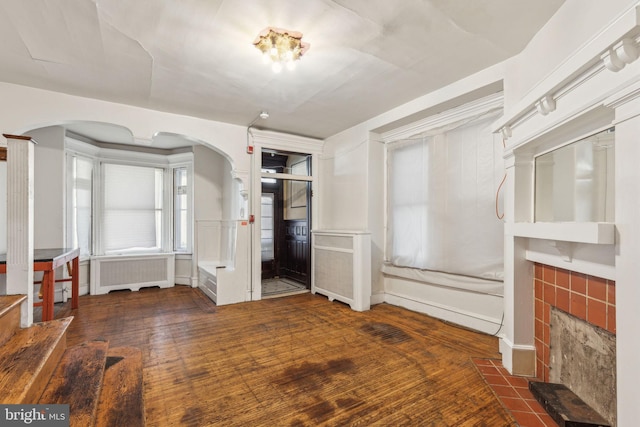 interior space featuring arched walkways, a tiled fireplace, radiator heating unit, and wood finished floors