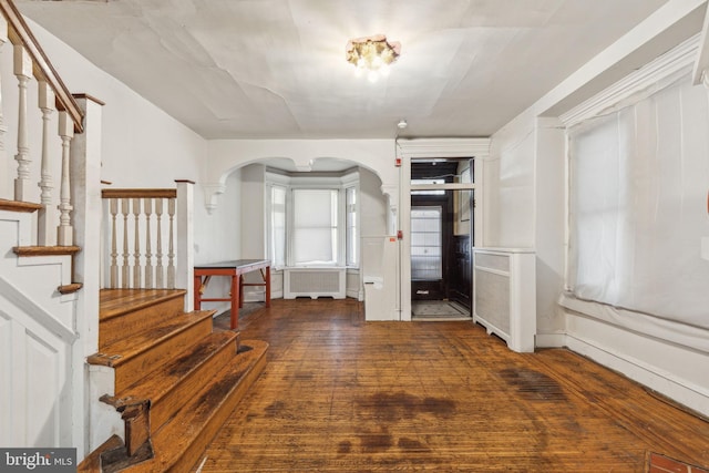 foyer entrance featuring radiator, hardwood / wood-style flooring, stairs, and arched walkways