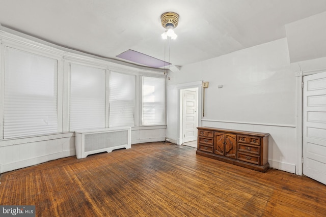 unfurnished living room featuring baseboards, wood finished floors, and radiator