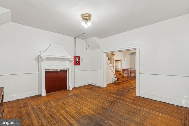 unfurnished living room with stairs, hardwood / wood-style floors, wainscoting, and lofted ceiling