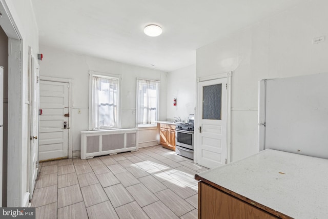 kitchen featuring wood finish floors, light countertops, freestanding refrigerator, radiator heating unit, and stainless steel range with gas stovetop