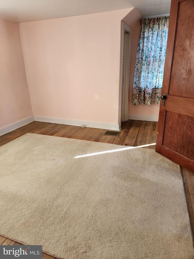 carpeted empty room featuring baseboards and wood-type flooring