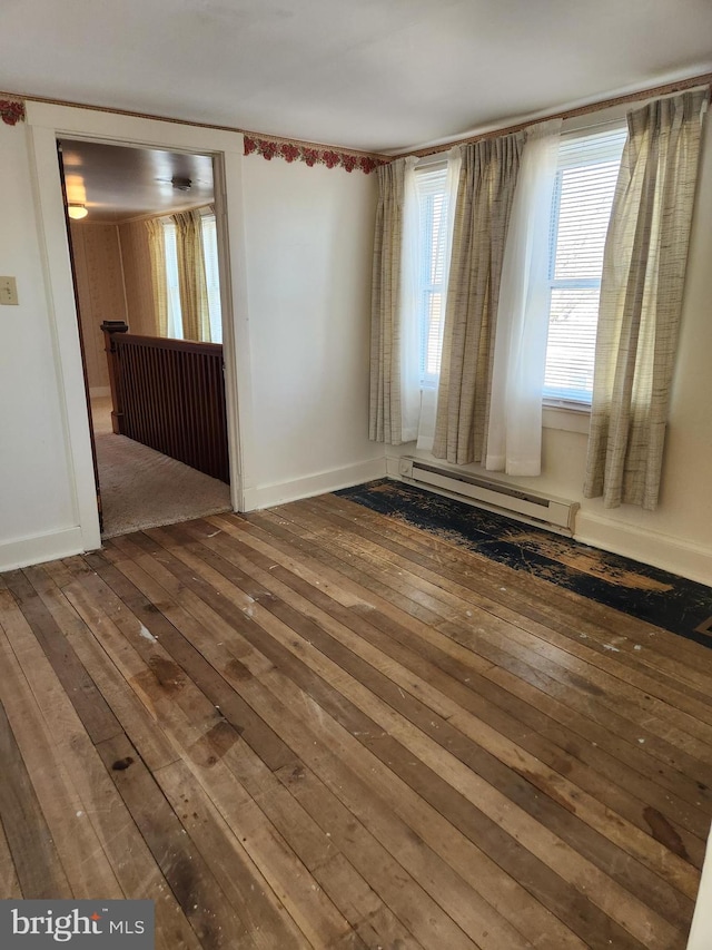 unfurnished room featuring baseboards, baseboard heating, and hardwood / wood-style flooring