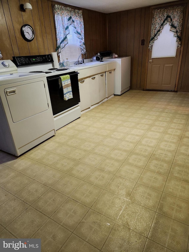 clothes washing area with a sink, separate washer and dryer, wooden walls, light floors, and laundry area