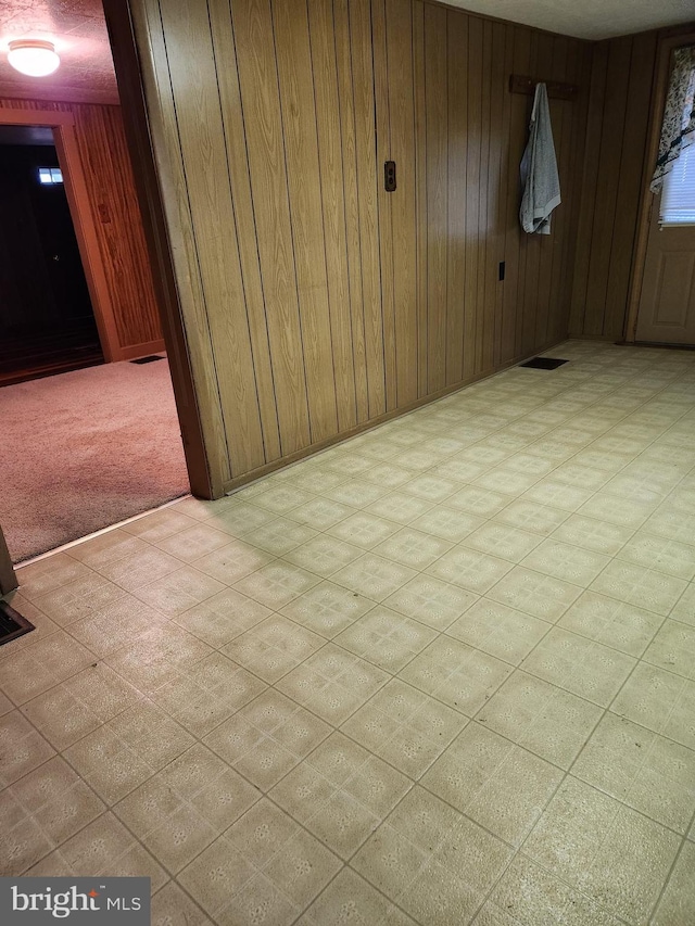 empty room featuring tile patterned floors, visible vents, and wood walls