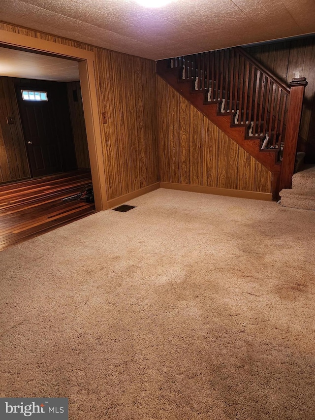 finished basement with stairway, visible vents, carpet floors, baseboards, and wood walls