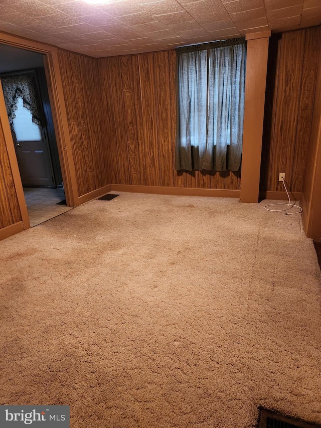 carpeted spare room featuring wooden walls and visible vents