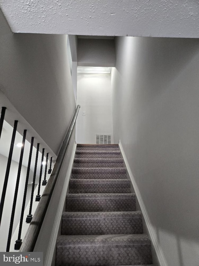 stairway featuring baseboards, visible vents, and a textured ceiling