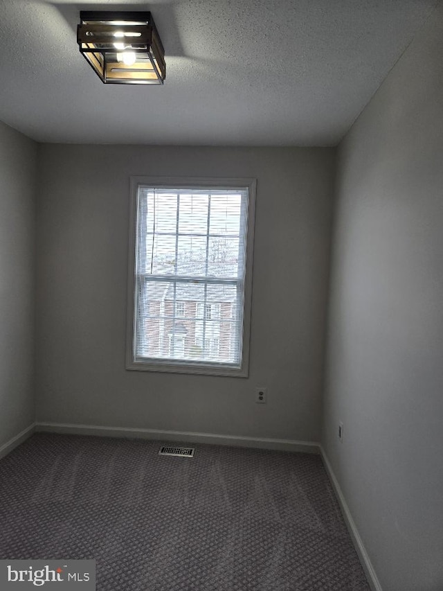 unfurnished room with baseboards, carpet, visible vents, and a textured ceiling