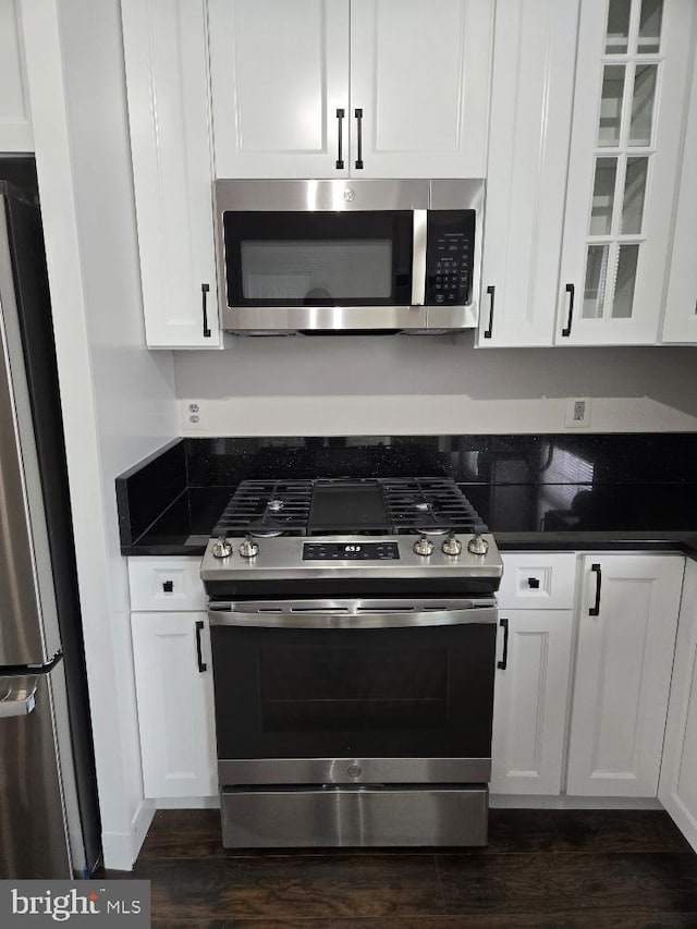 kitchen with dark wood-style floors, stainless steel appliances, dark countertops, and white cabinetry