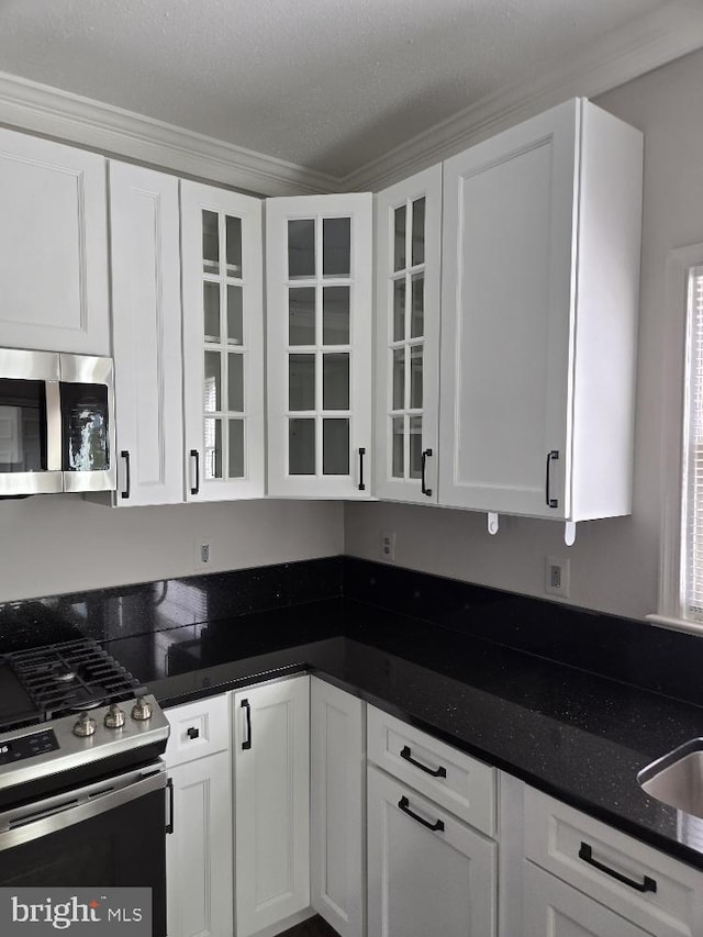 kitchen with white cabinets, glass insert cabinets, stainless steel appliances, and dark stone counters