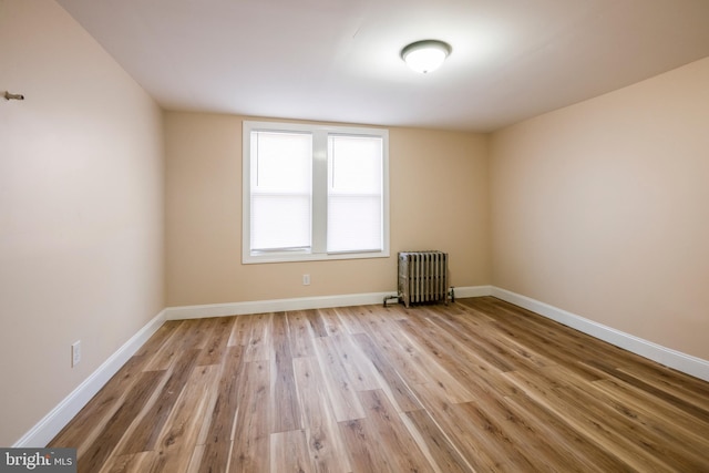 unfurnished room featuring baseboards, wood finished floors, and radiator heating unit