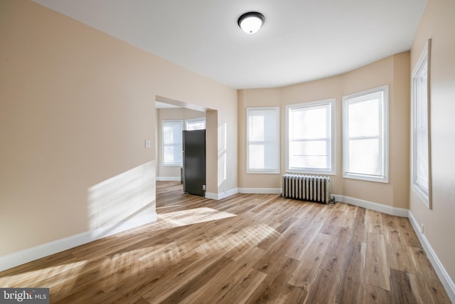 empty room with radiator, baseboards, and wood finished floors