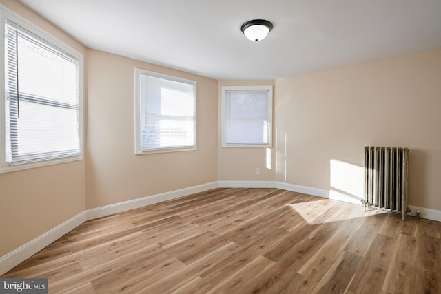 spare room with radiator heating unit, light wood-style floors, plenty of natural light, and baseboards