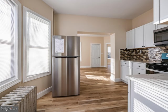 kitchen featuring backsplash, radiator heating unit, stainless steel appliances, light wood-style floors, and white cabinetry