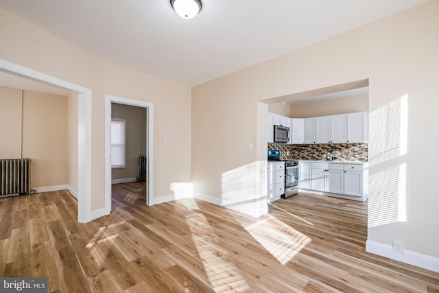 interior space with radiator heating unit, light countertops, appliances with stainless steel finishes, white cabinetry, and tasteful backsplash