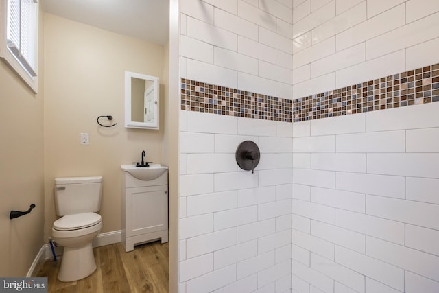 full bathroom featuring toilet, wood finished floors, a tile shower, baseboards, and vanity