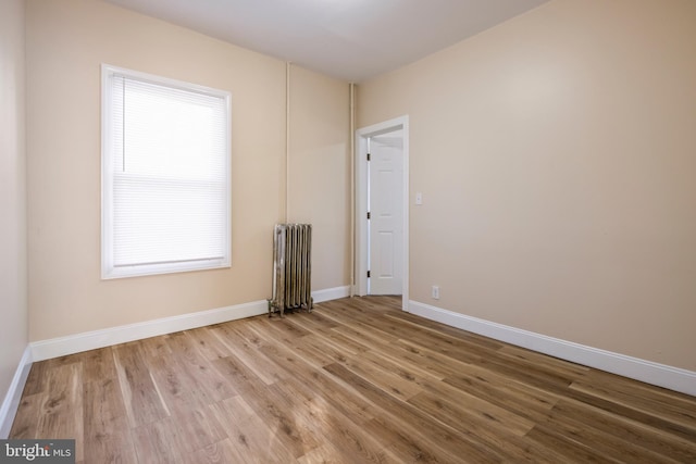 empty room featuring radiator heating unit, baseboards, and wood finished floors