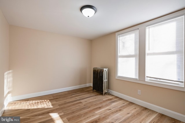 spare room featuring light wood-style floors, a healthy amount of sunlight, radiator heating unit, and baseboards