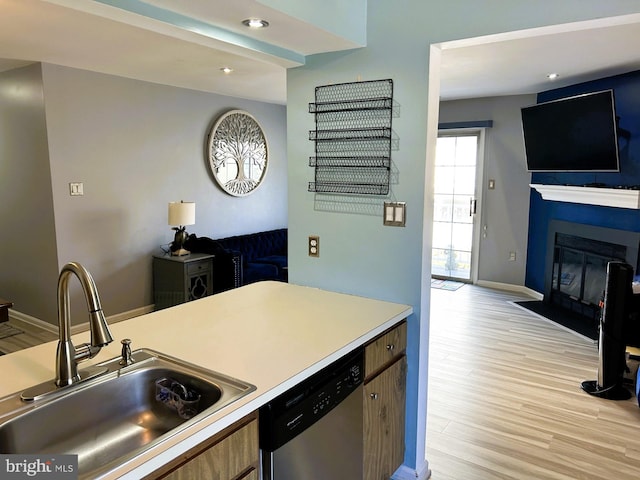 kitchen with light wood-style flooring, a sink, open floor plan, dishwasher, and a glass covered fireplace