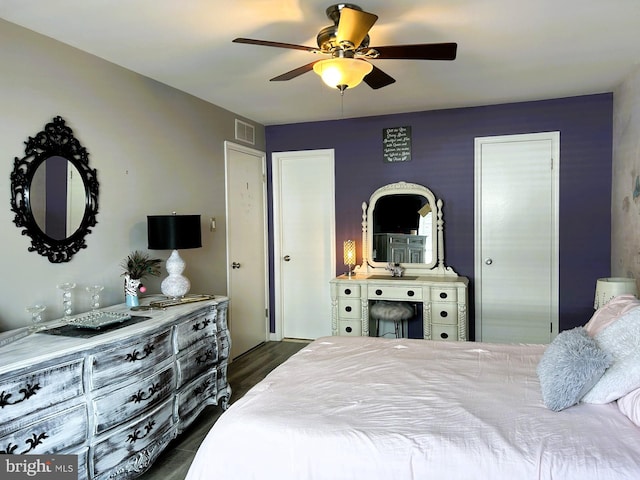 bedroom with ceiling fan, visible vents, dark wood finished floors, and multiple closets