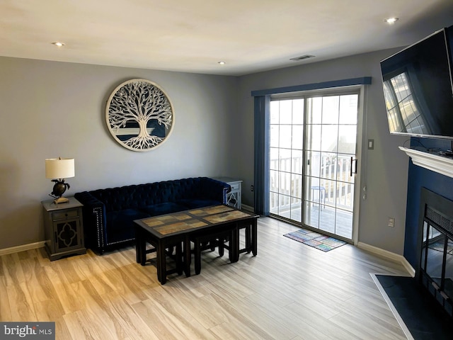 living area with light wood finished floors, visible vents, baseboards, a fireplace with flush hearth, and recessed lighting