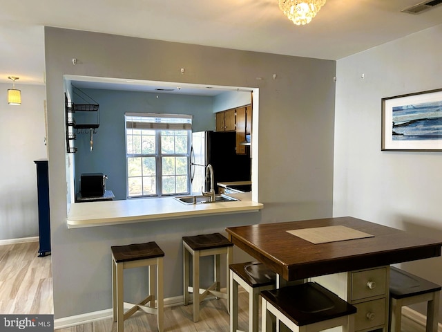 kitchen featuring light wood finished floors, visible vents, freestanding refrigerator, a peninsula, and a sink