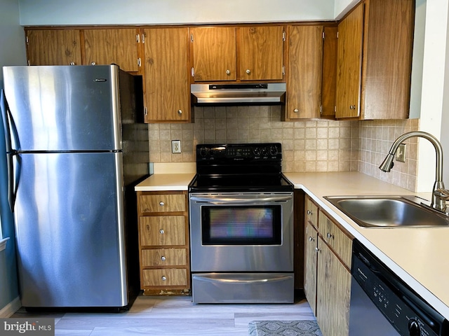 kitchen featuring under cabinet range hood, stainless steel appliances, brown cabinetry, and a sink