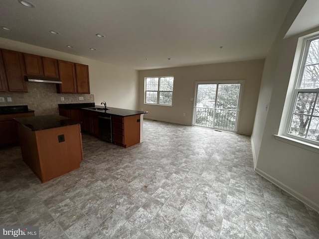 kitchen featuring black dishwasher, dark countertops, open floor plan, a sink, and under cabinet range hood