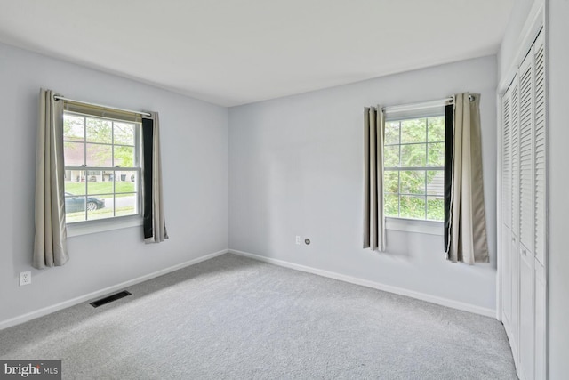unfurnished room featuring carpet floors, visible vents, and a wealth of natural light