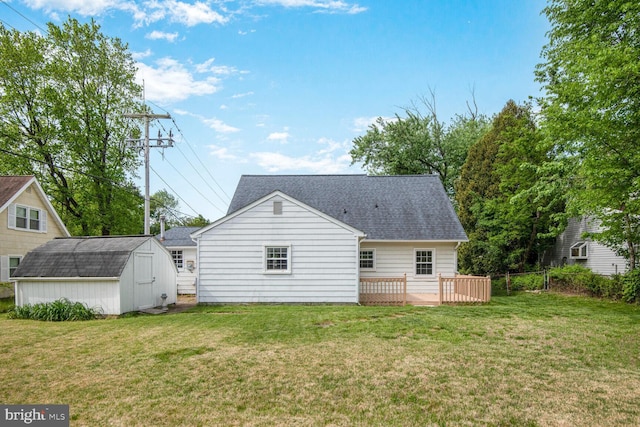 rear view of property featuring roof with shingles, a storage shed, a deck, an outbuilding, and a lawn