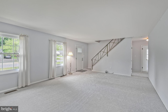 unfurnished living room with carpet floors, baseboards, stairs, and visible vents