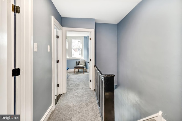 corridor featuring carpet floors, baseboards, and an upstairs landing