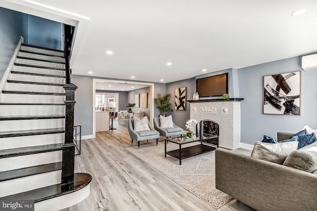 living area featuring light wood-style flooring, stairway, a wall mounted air conditioner, a fireplace, and recessed lighting