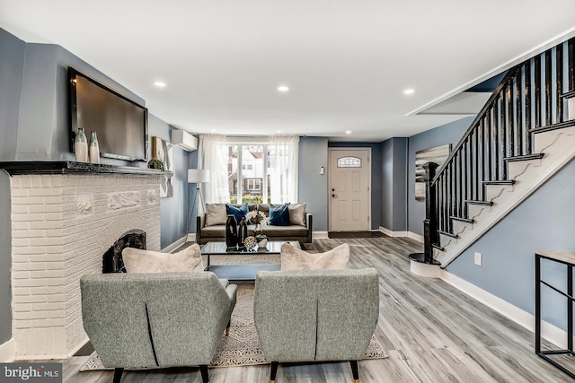 living area with a fireplace, a wall mounted AC, wood finished floors, baseboards, and stairs