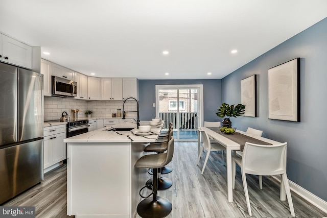 kitchen with a breakfast bar area, stainless steel appliances, light wood-style flooring, decorative backsplash, and a sink