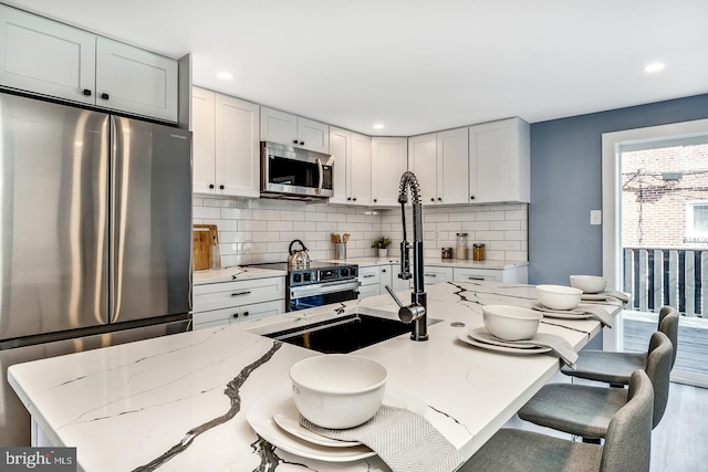 kitchen with light stone counters, recessed lighting, decorative backsplash, appliances with stainless steel finishes, and a kitchen breakfast bar