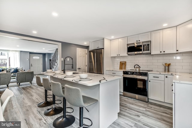 kitchen featuring light wood finished floors, backsplash, appliances with stainless steel finishes, open floor plan, and a sink